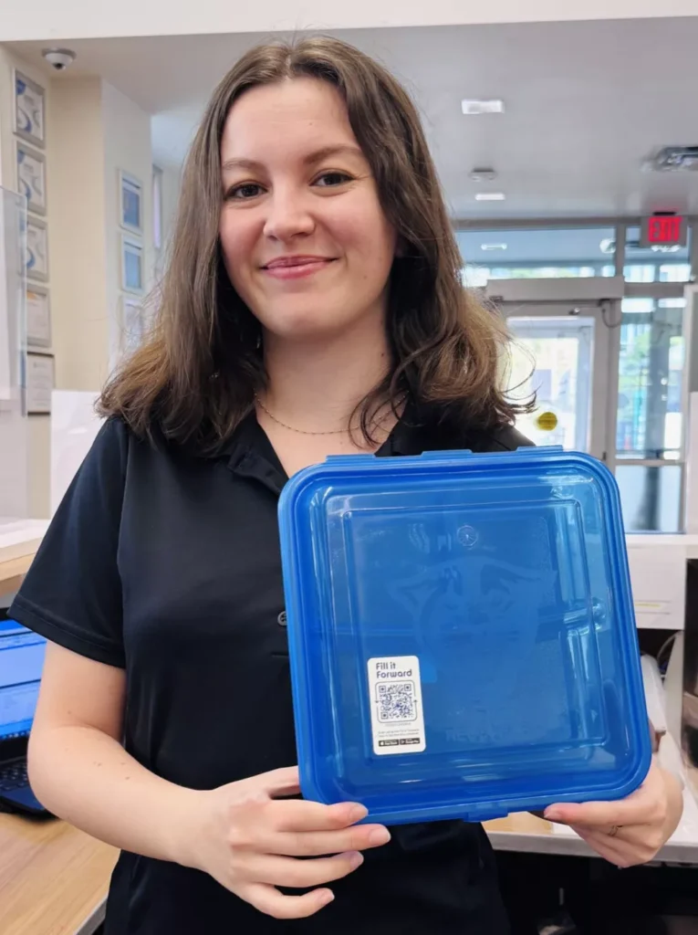 A student from GSU holding a blue reusable container with with a Fill it Forward Borrow sticker on it.